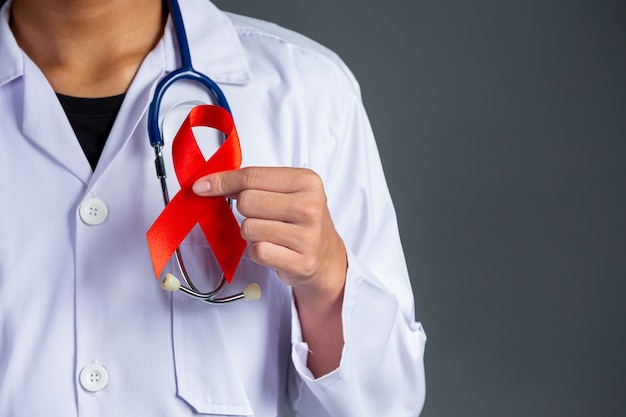 Foto gratuita il medico tiene in mano un nastro rosso, la consapevolezza dell'hiv, la giornata mondiale contro l'aids e la giornata mondiale della salute sessuale.