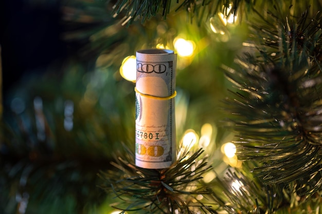 Foto gratuita una banconota di un dollaro appesa all'albero di natale con luci bokeh