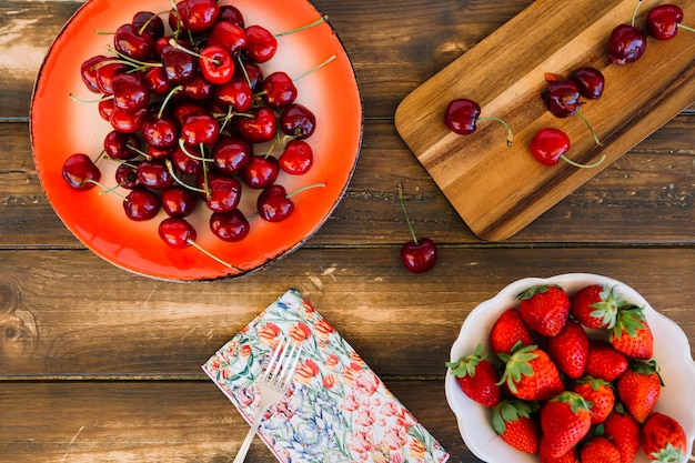 Foto gratuita vista elevata di fragole e ciliegie su fondo in legno