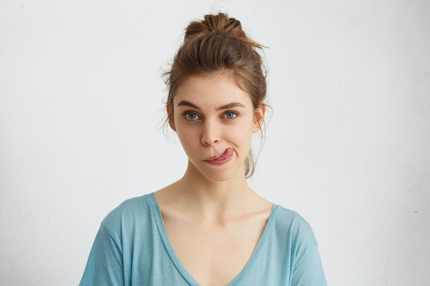 Foto gratuita donna divertente con ciambella capelli biondi e affascinanti occhi azzurri che hanno gioia mentre mostra la lingua.