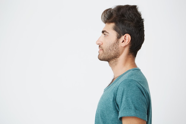 Foto gratuita ritratto a mezza faccia di un bellissimo uomo spagnolo, in casual t-shirt blu, con capelli e barba alla moda, mostrando il suo profilo e guardando a sinistra. copia spazio.