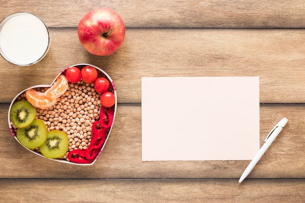 Foto gratuita verdure sane frutta; latte con carta bianca e penna sul tavolo di legno