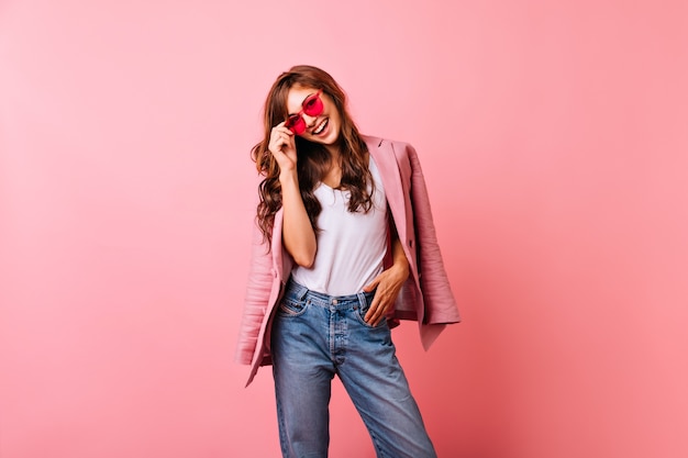 Foto gratuita signora ottimista dello zenzero in occhiali da sole luminosi che ride. sorridente splendida ragazza in jeans in posa sul rosa.