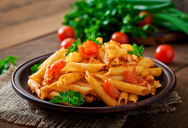 Foto gratuita pasta di penne in salsa di pomodoro con pollo e pomodori su un tavolo di legno