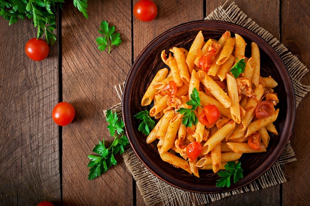 Foto gratuita pasta di penne in salsa di pomodoro con pollo e pomodori su un tavolo di legno