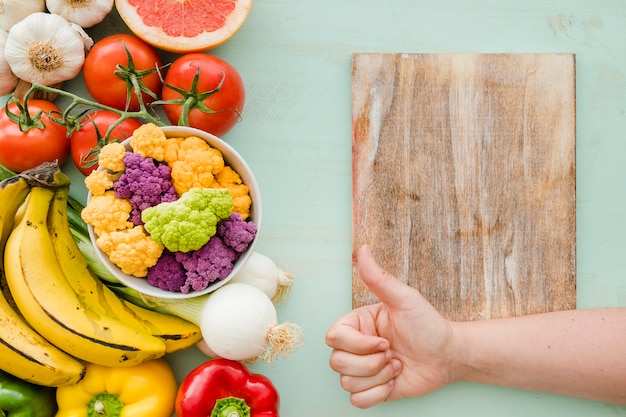 Foto gratuita una persona che mostra thumbsup firma sul tavolo e sul cibo fresco sano