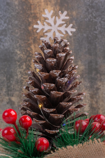 Foto gratuita pigna decorata con bacche di agrifoglio e fiocco di neve sul tavolo bianco.