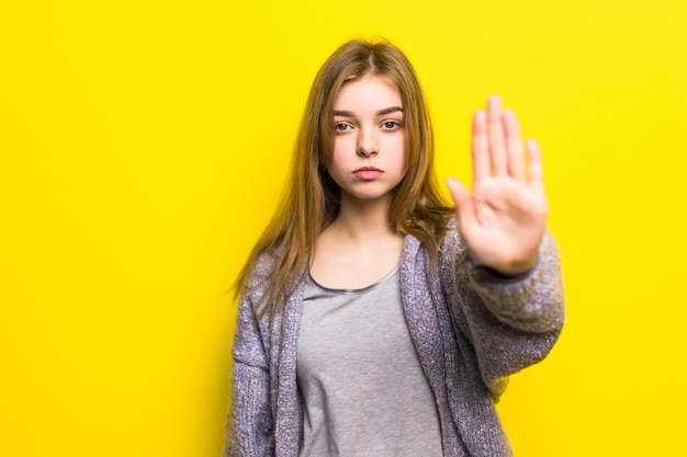 Foto gratuita ritratto di una donna abbastanza sorridente isolata su una parete gialla. ragazza che fa il gesto di arresto con la mano