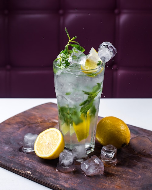 Foto gratuita vista laterale del cocktail mojito con ghiaccio e limone su una tavola di legno