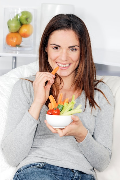 Foto gratuita donna sorridente sul divano con insalata di verdure