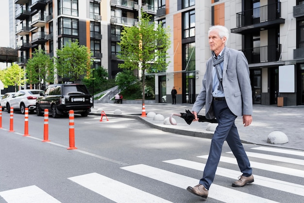 Foto gratuita elegante uomo anziano in città che attraversa la strada mentre tiene l'ombrello