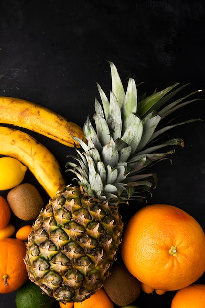 Foto gratuita vista dall'alto di agrumi come banana ananas arancione e altri sulla superficie nera