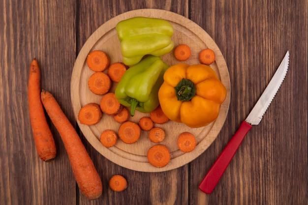 Foto gratuita vista dall'alto di peperoni colorati su una tavola di cucina in legno con carote tritate con coltello con carote isolate su una superficie di legno