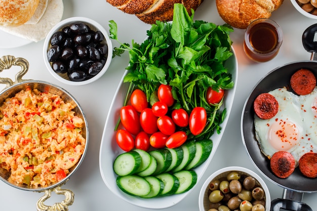 Foto gratuita vista dall'alto deliziosi pasti in padella e pentola con insalata, sottaceti, bagel turco, una tazza di tè sulla superficie bianca