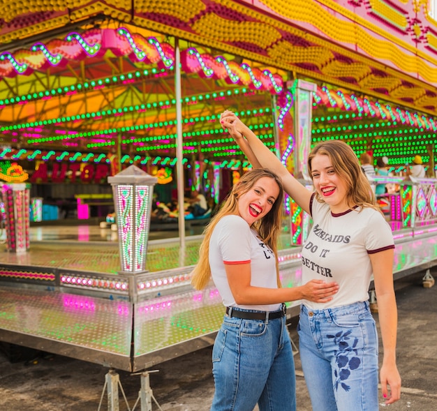 Foto gratuita due amici femminili felici che alzano le loro armi al parco di divertimenti