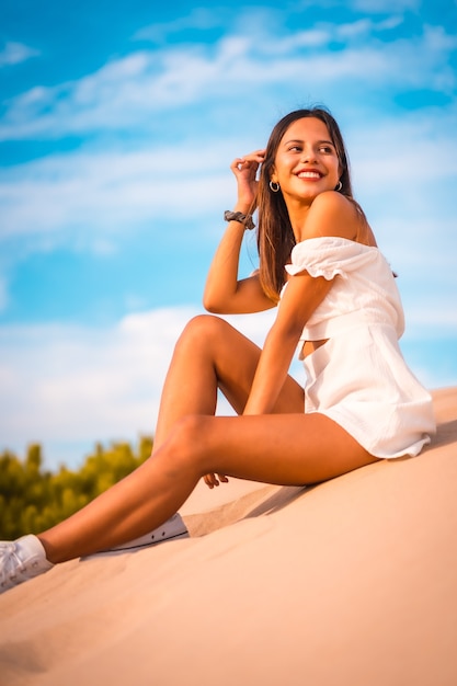 Foto gratuita ripresa verticale di una giovane donna caucasica bruna che si gode una vacanza in spiaggia con un vestito bianco