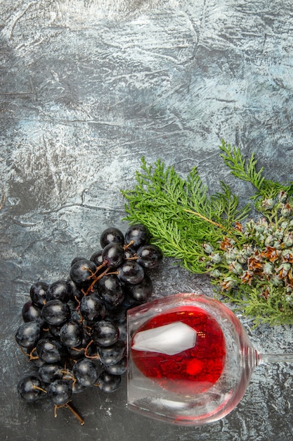 Foto gratuita vista verticale del bicchiere di vino rosso caduto e un mucchio di rami di abete d'uva nera su sfondo di ghiaccio