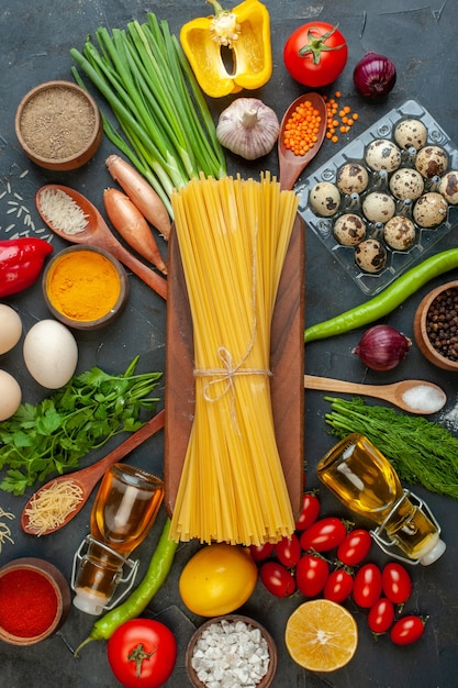 Foto gratuita vista verticale degli spaghetti su una tavola di legno tra le uova di verdure biologiche, il pepe della bottiglia di olio caduto sul nero