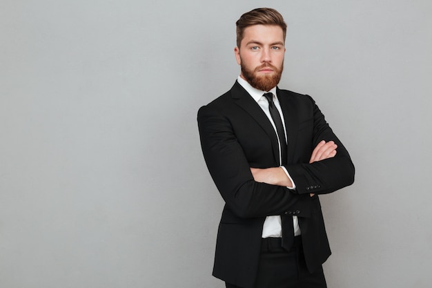 Photo gratuite confiant jeune homme d'affaires en costume debout avec les bras croisés