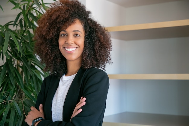 Photo gratuite femme d'affaires bouclés afro-américaine debout avec les mains jointes. portrait d'employeur de bureau jeune jolie femme confiant réussi en costume posant au travail. concept d'entreprise, d'entreprise et de gestion