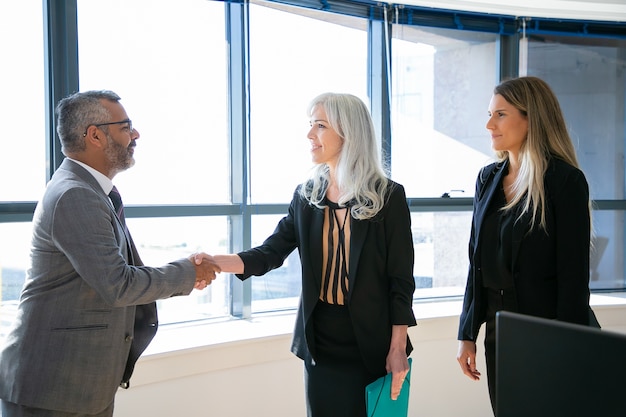 Photo gratuite les gens d'affaires de contenu saluent, rencontrent et sourient. succès du pdg indien en lunettes de poignée de main avec une femme d'affaires aux cheveux gris, lui parlant et la regardant. concept d'entreprise et de partenariat