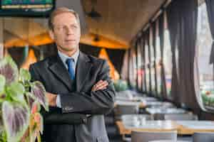 Photo gratuite portrait d'un homme d'affaires mature avec les bras croisés, debout dans le restaurant