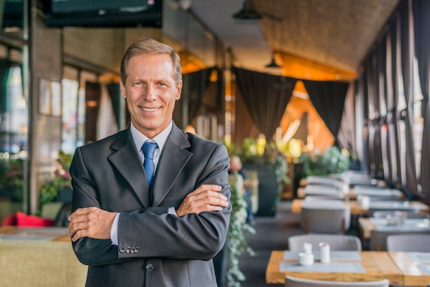 Photo gratuite portrait d'un homme d'affaires prospère, debout dans un restaurant avec bras croisé