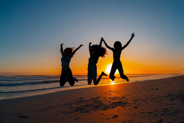 Photo gratuite silhouettes complètes de personnes sautant au coucher du soleil