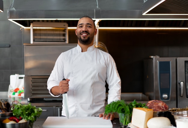 Photo beau jeune chef africain debout dans une cuisine professionnelle au restaurant préparant un repas de viande et de légumes au fromage. portrait d'homme en uniforme de cuisinier. concept de saine alimentation.