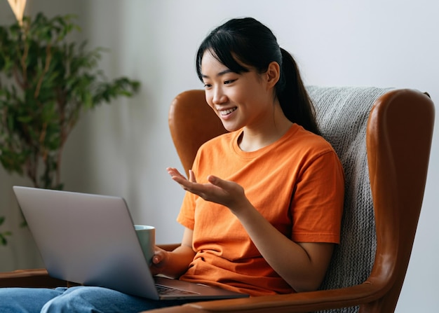 Foto una ragazza asiatica si siede su una sedia parlando con un portatile e tenendo una tazza di caffè