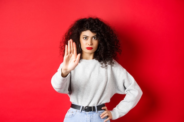 Foto donna fiduciosa tesa allunga la mano per dire stop, disapprovare l'azione e proibirla, non fare alcun gesto, stare su sfondo rosso e proibire qualcosa.