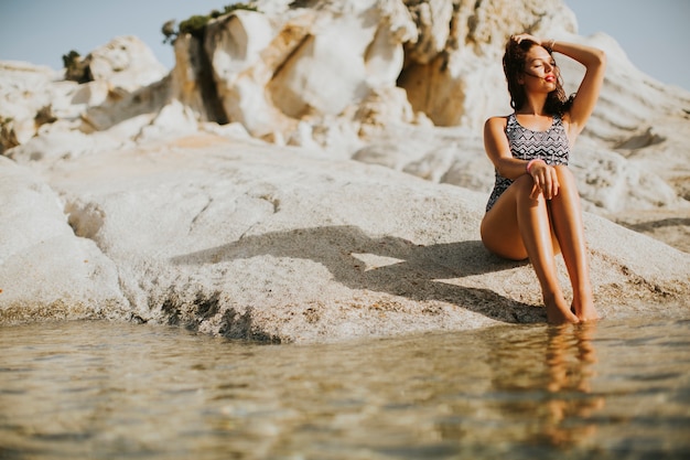 Foto giovane donna graziosa che si siede sulla riva rocciosa dal mare