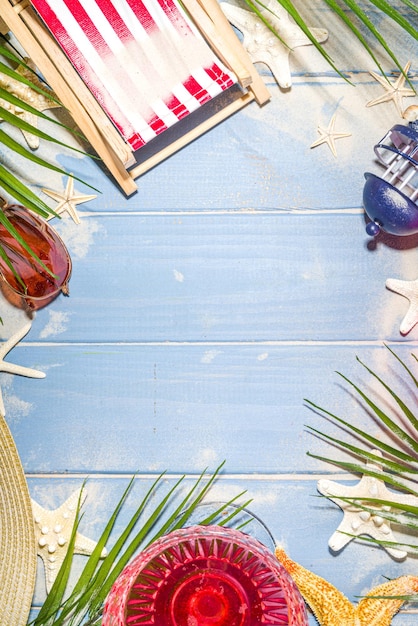 Foto vacanze estive in spiaggia e sfondo di viaggio con sedia a sdraio, salvagente, cocktail, foglie tropicali, sabbia, occhiali da sole, stelle marine conchiglie. il sole blu ha illuminato lo spazio della copia del fondo di legno