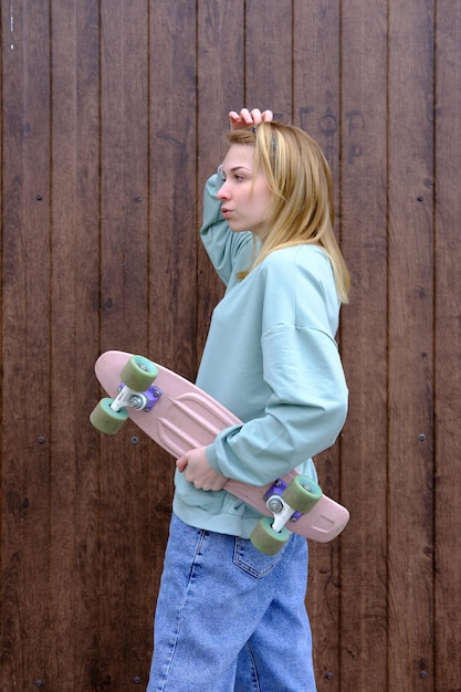 Foto ragazza adolescente con uno skateboard nelle mani sullo sfondo di un muro di legno