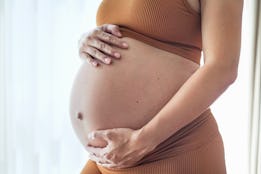 Close-up side view shot of unrecognizable pregnant woman rubbing her big belly