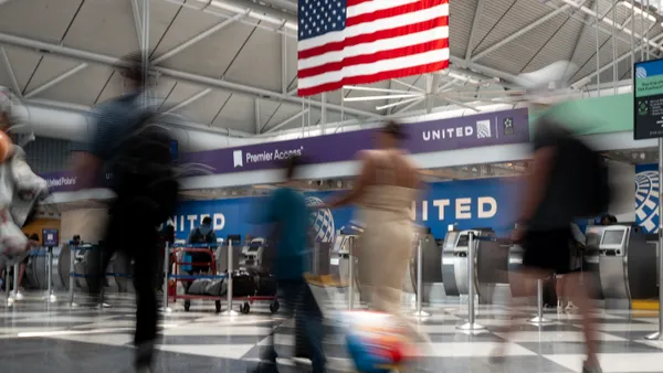 Travelers walk through an airport terminal that is displaying an American flag.