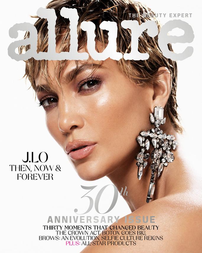 Jennifer Lopez, musician, actor, and founder of JLo Beauty, looking over her shoulder into the camera for Allure Magazine’s March 2021 cover interview. Her hair is short and she wears a silver chandelier earring. Text on image reads: J.Lo Then, Now, & Forever. Photographed by Daniella Midenge.