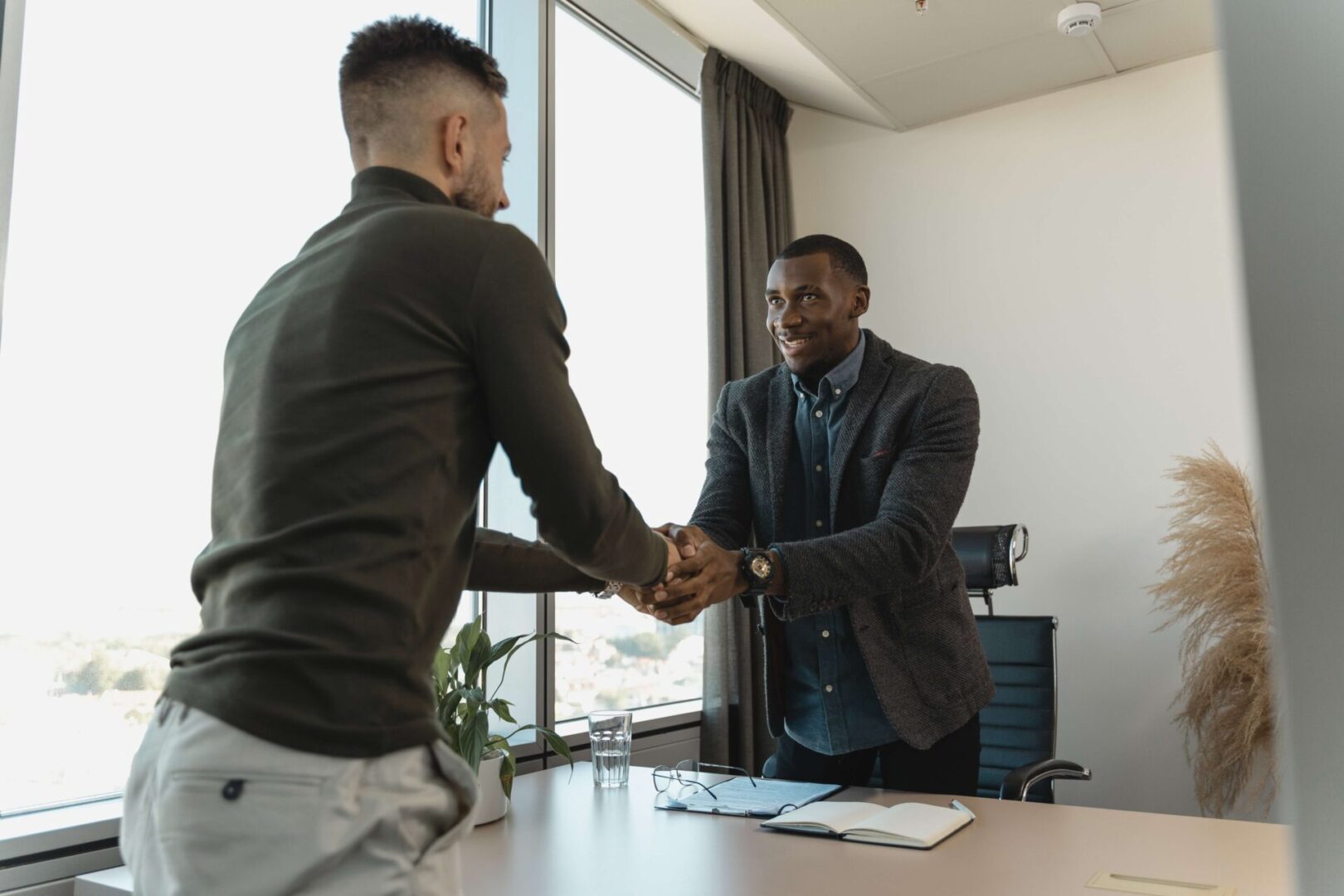 Two men shaking hands in front of a window.