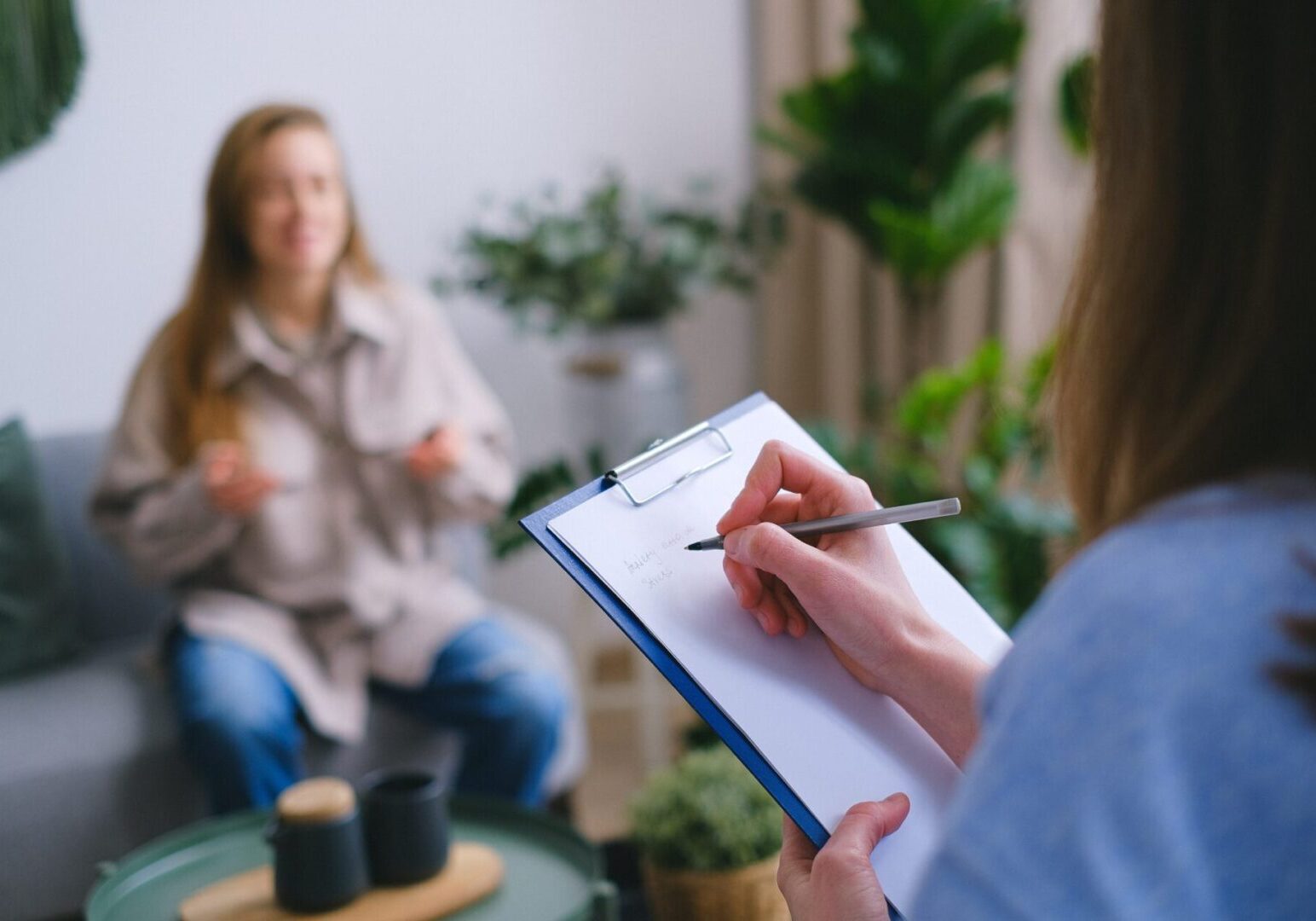 A person writing on paper in front of another person.