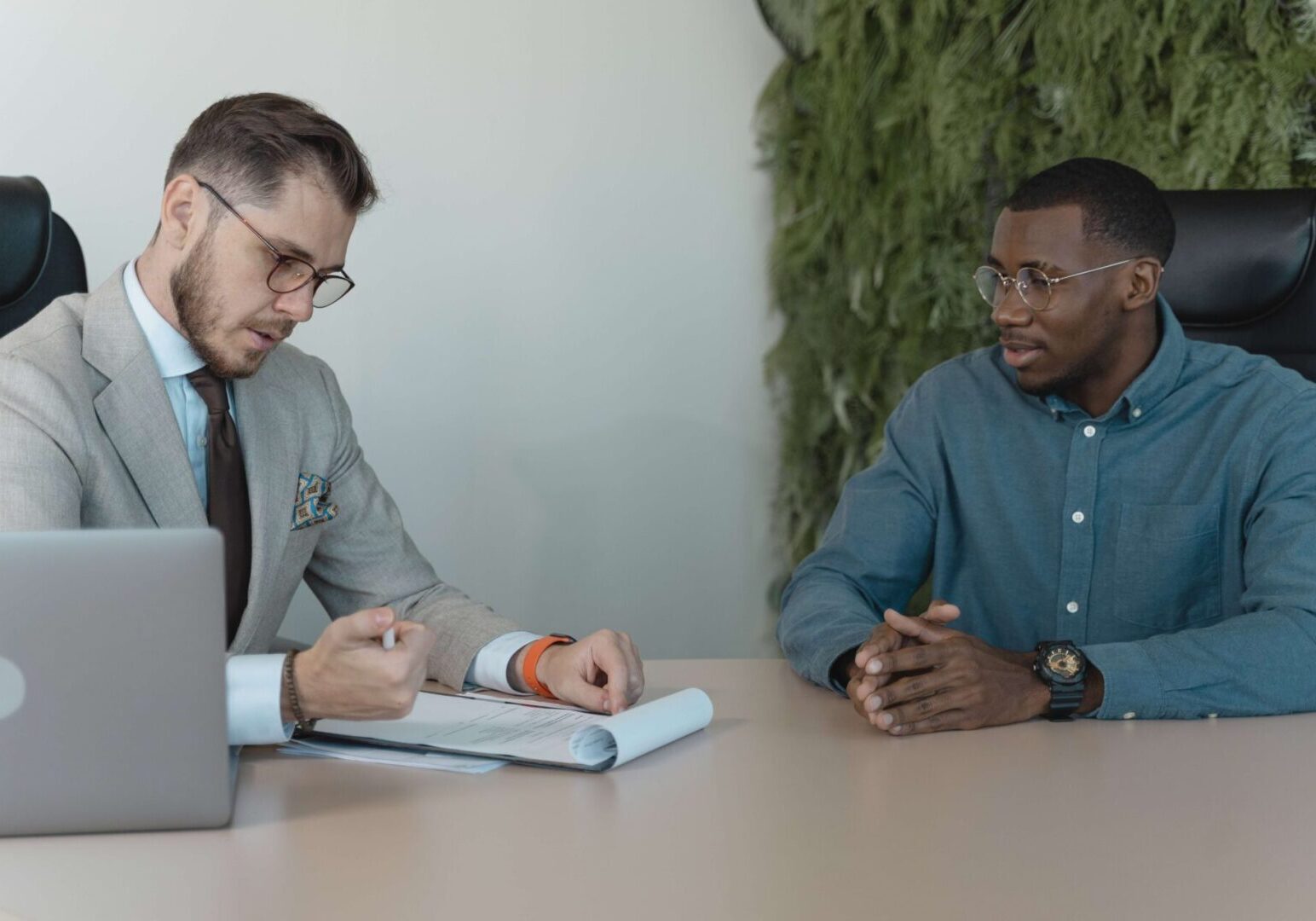 Two men sitting at a table with one man writing on the paper.