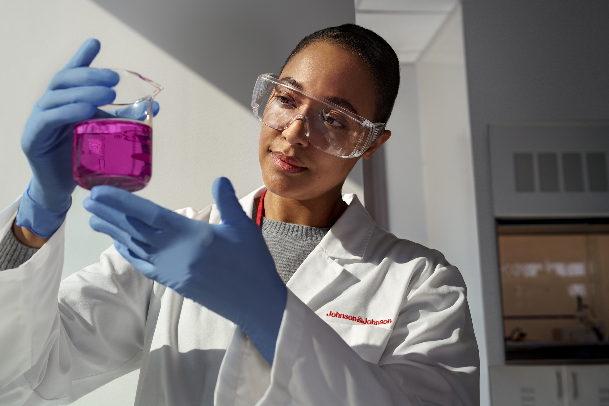 Black female scientist in full PPE holding a beaker filled with bright purple liquid 