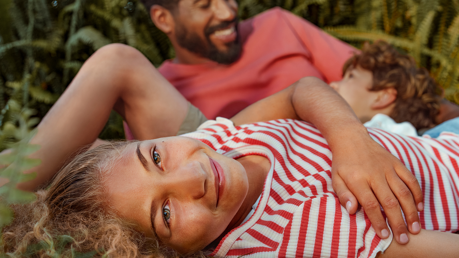 A child in a striped sweater smiling while laying in the grass 