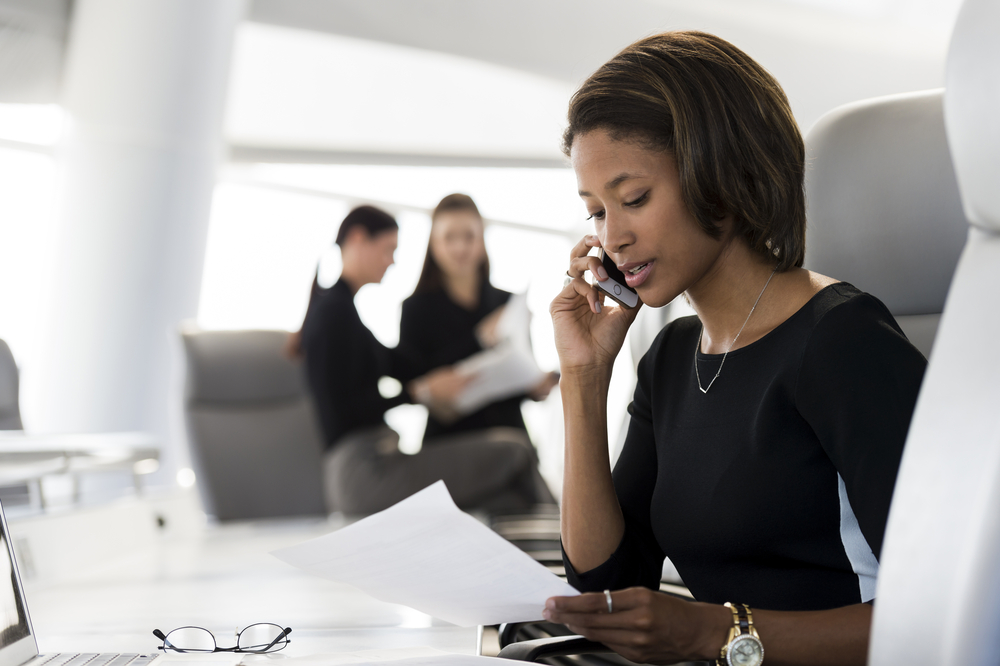 A black business woman speaking on a smartphone at her desk 