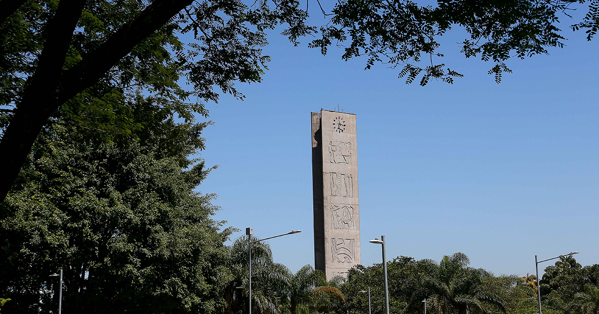 Foto mostra paisagem com árvores e, ao centro, a Torre do Relógio, na Praça do Relógio do campus Butantã da Universidade de São Paulo