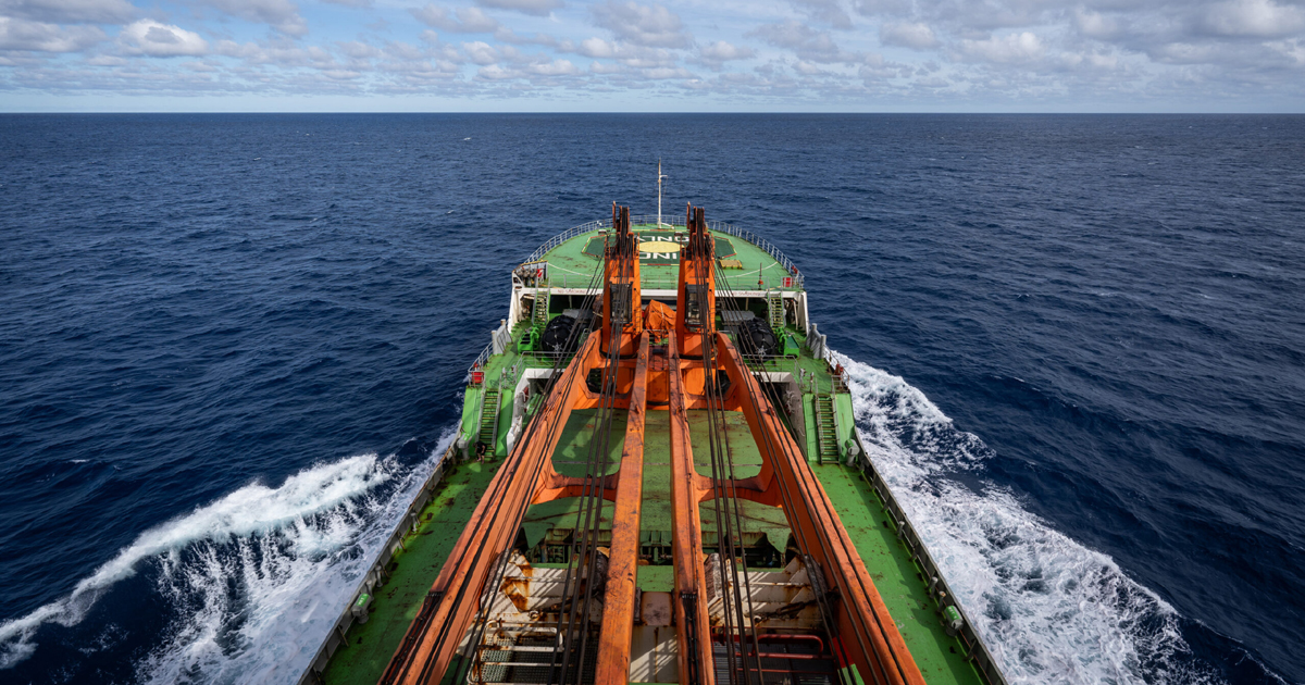 Imagem aérea da proa de um navio de cor verde, com ferragens cor de laranja, navegando rumo ao Oceano Glacial Antártico