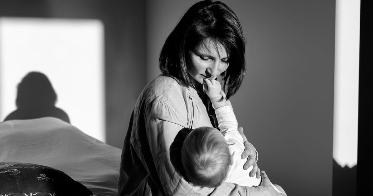 Imagem: Mulher branca de cabelos pretos segura um bebê no colo. Foto em preto e branco