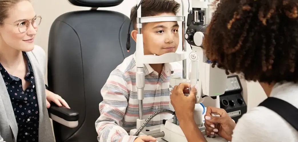 Young boy getting his eyes checked out by a doctor as his guardian sits nearby