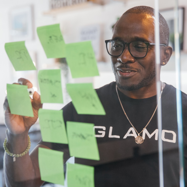 A person writing on a glass wall with sticky notes