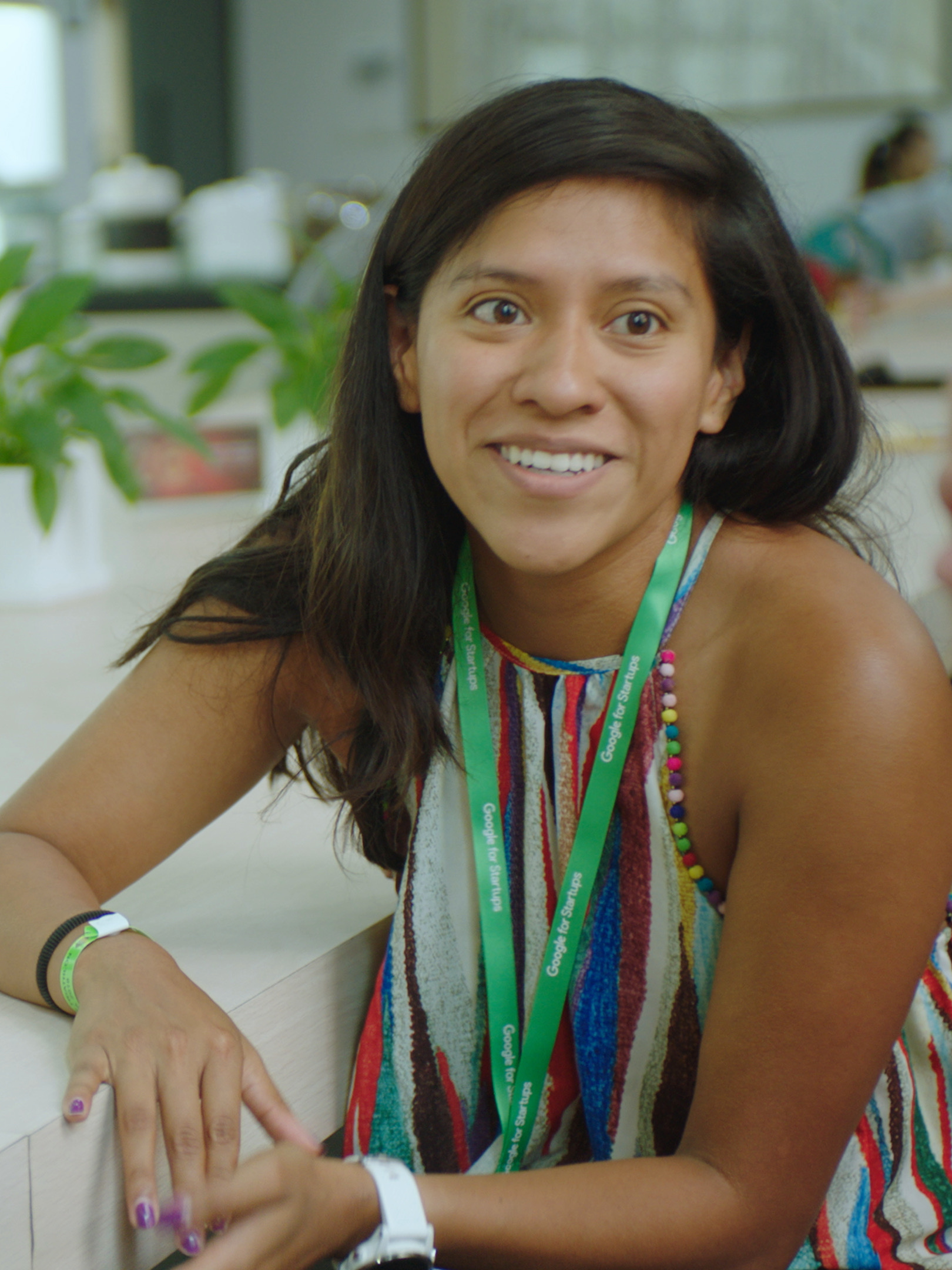 a woman smiling while sitting on a chair with her elbow on the table