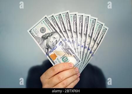 1000 dollars in 100 bills in a man's hand close-up on a dark background. Hands holding dollar cash Stock Photo